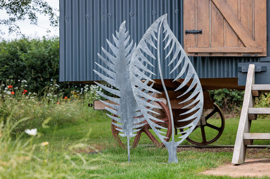 Decorative metal leaf sculptures in a garden setting with a wooden shed and wheelbarrow in the background.