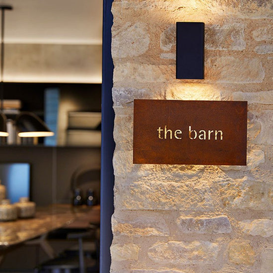 Rust-colored metal sign with 'the barn' on a stone wall.
